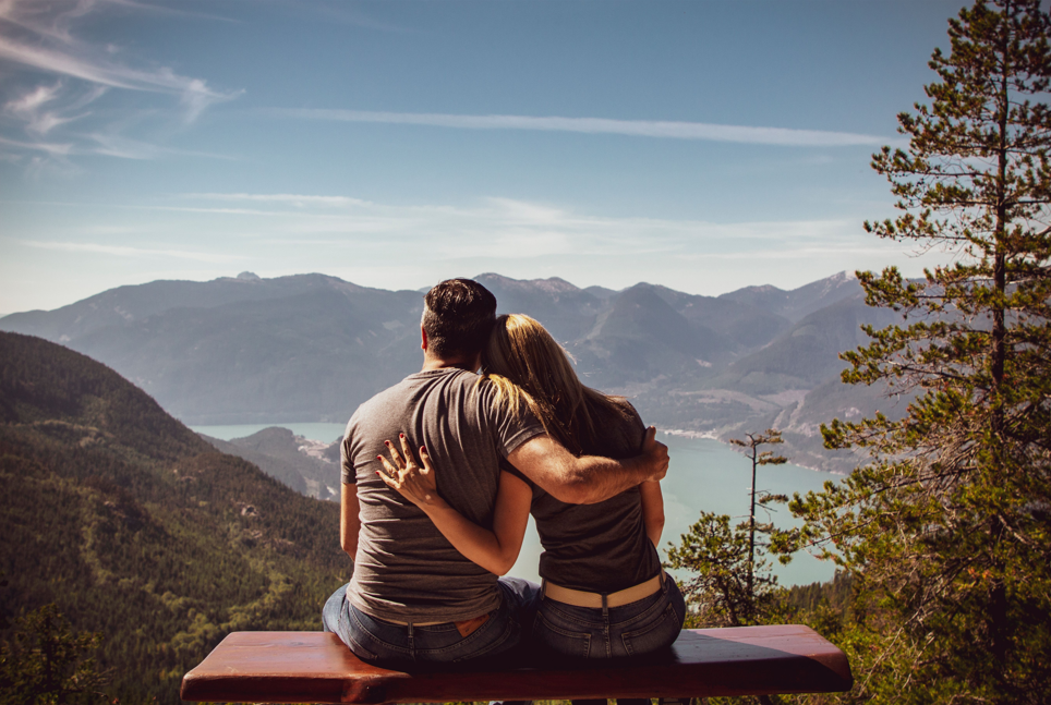 Couple sitting on a bench overlooking mountains and a lake